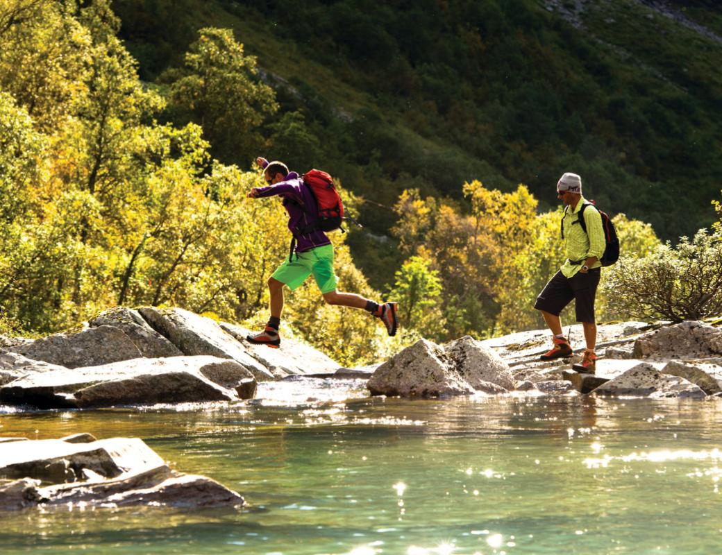 Two young men on a hike in the forest, jumping over some water